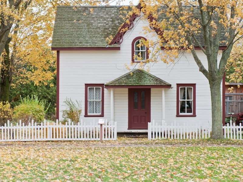 Two-storey Winnipeg character home with white siding, burgundy trim, and mature autumn maple trees