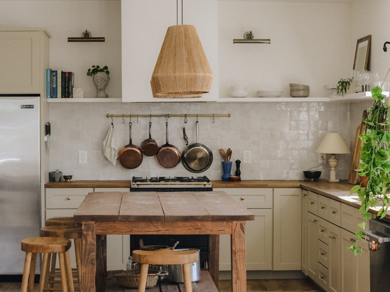 Character home interior with rustic wood island, copper pots, woven pendant lamp, and sage-painted cabinetry